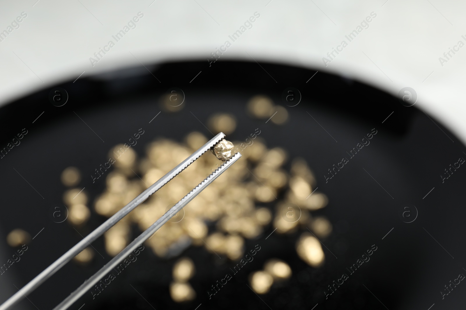 Photo of Tweezers with gold nugget against blurred background, closeup. Space for text