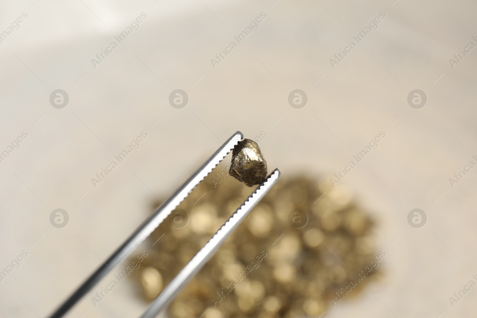 Photo of Tweezers with gold nugget against blurred background, closeup