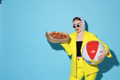 Photo of Stylish woman with delicious pizza and inflatable ball on light blue background, space for text