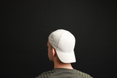 Photo of Man in stylish baseball cap on black background, back view. Mockup for design