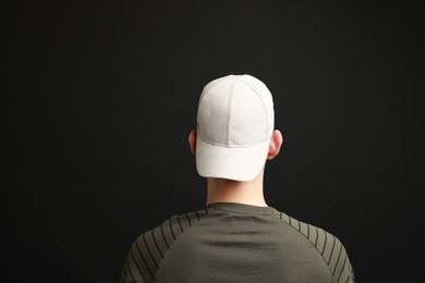 Photo of Man in stylish baseball cap on black background, back view. Mockup for design