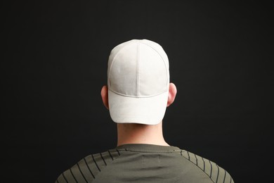 Photo of Man in stylish baseball cap on black background, back view. Mockup for design