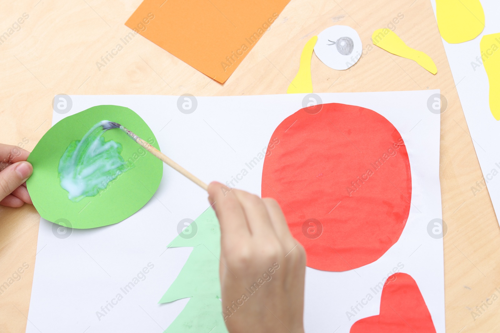 Photo of Girl applying glue onto paper figure for her creative project at table indoors, above view. Art and craft