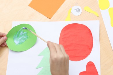 Girl applying glue onto paper figure for her creative project at table indoors, above view. Art and craft