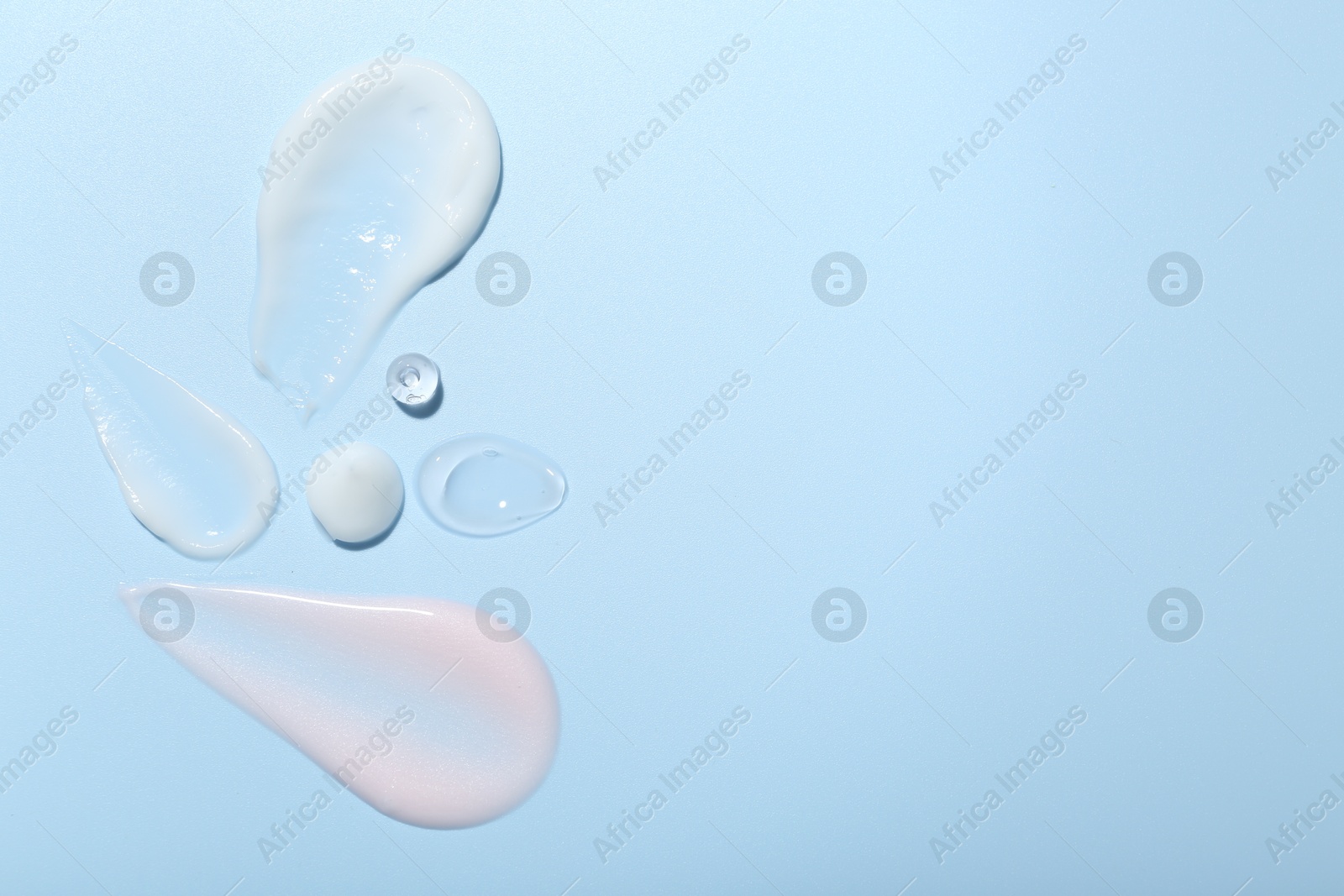 Photo of Cream and gel samples on light blue background, top view. Space for text