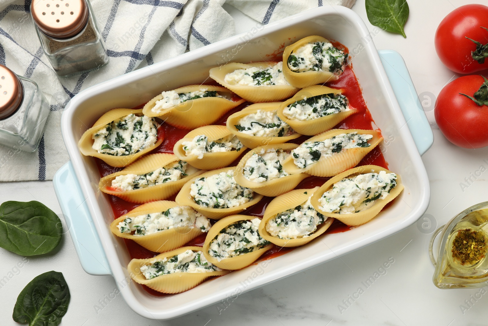 Photo of Delicious conchiglie pasta with ricotta cheese, spinach and tomato sauce in baking dish on white marble table, flat lay