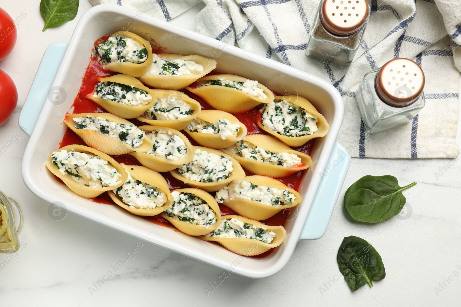 Photo of Delicious conchiglie pasta with ricotta cheese, spinach and tomato sauce in baking dish on white marble table, flat lay