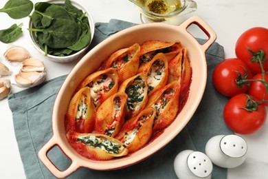 Photo of Delicious conchiglie pasta with ricotta cheese, spinach and tomato sauce in baking dish on white table, flat lay