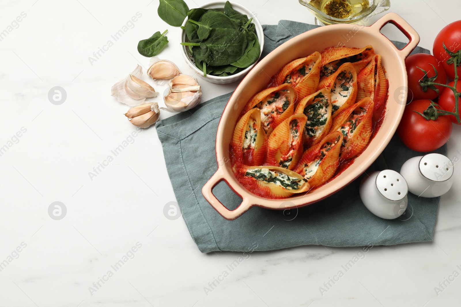 Photo of Delicious conchiglie pasta with ricotta cheese, spinach and tomato sauce in baking dish on white marble table, flat lay. Space for text