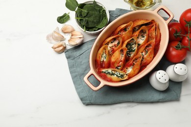 Photo of Delicious conchiglie pasta with ricotta cheese, spinach and tomato sauce in baking dish on white marble table, flat lay. Space for text