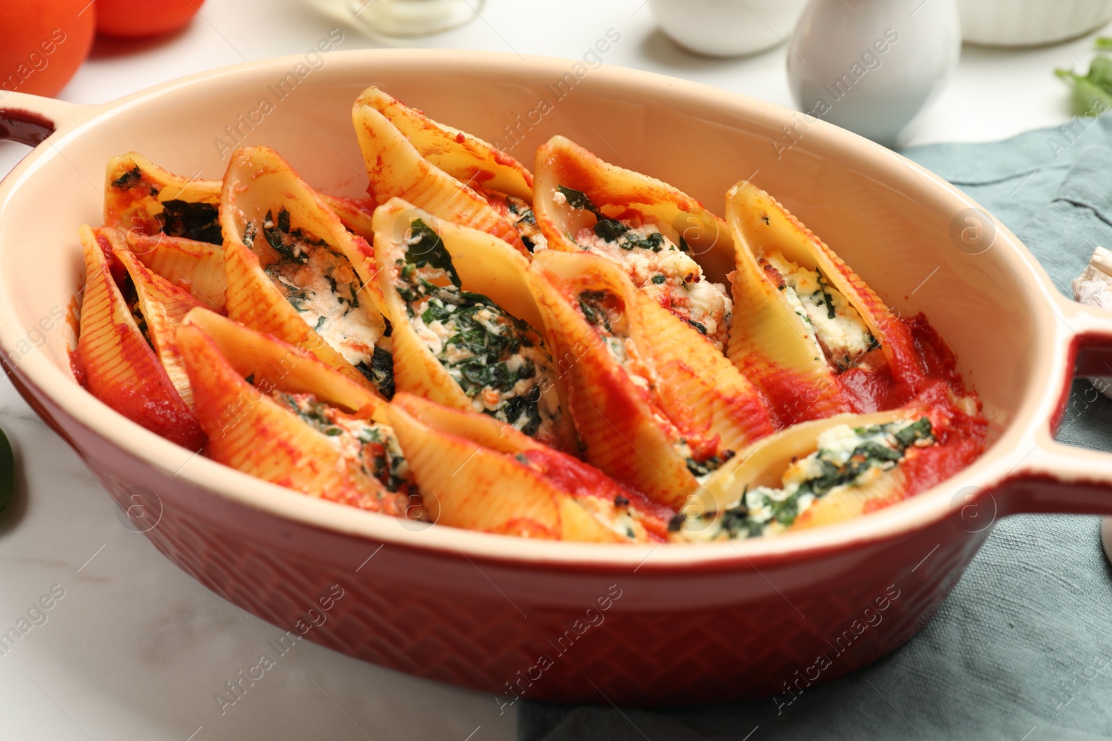 Photo of Delicious conchiglie pasta with ricotta cheese, spinach and tomato sauce in baking dish on white table, closeup