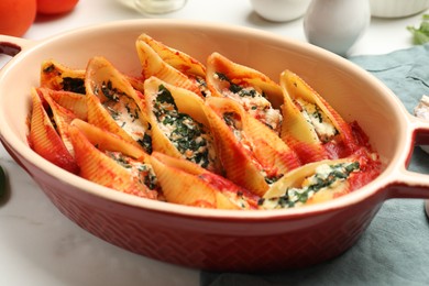 Photo of Delicious conchiglie pasta with ricotta cheese, spinach and tomato sauce in baking dish on white table, closeup