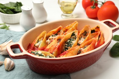 Photo of Delicious conchiglie pasta with ricotta cheese, spinach and tomato sauce in baking dish on white table, closeup