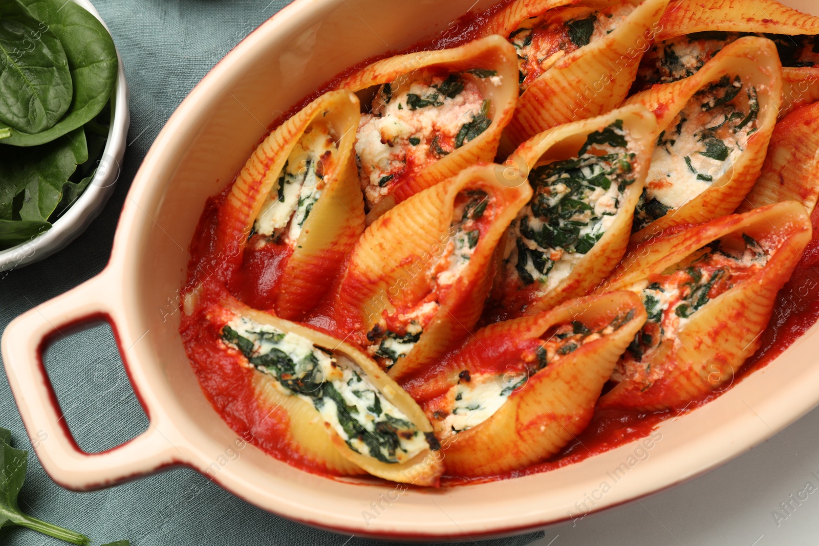 Photo of Delicious conchiglie pasta with ricotta cheese, spinach and tomato sauce in baking dish on white table, top view