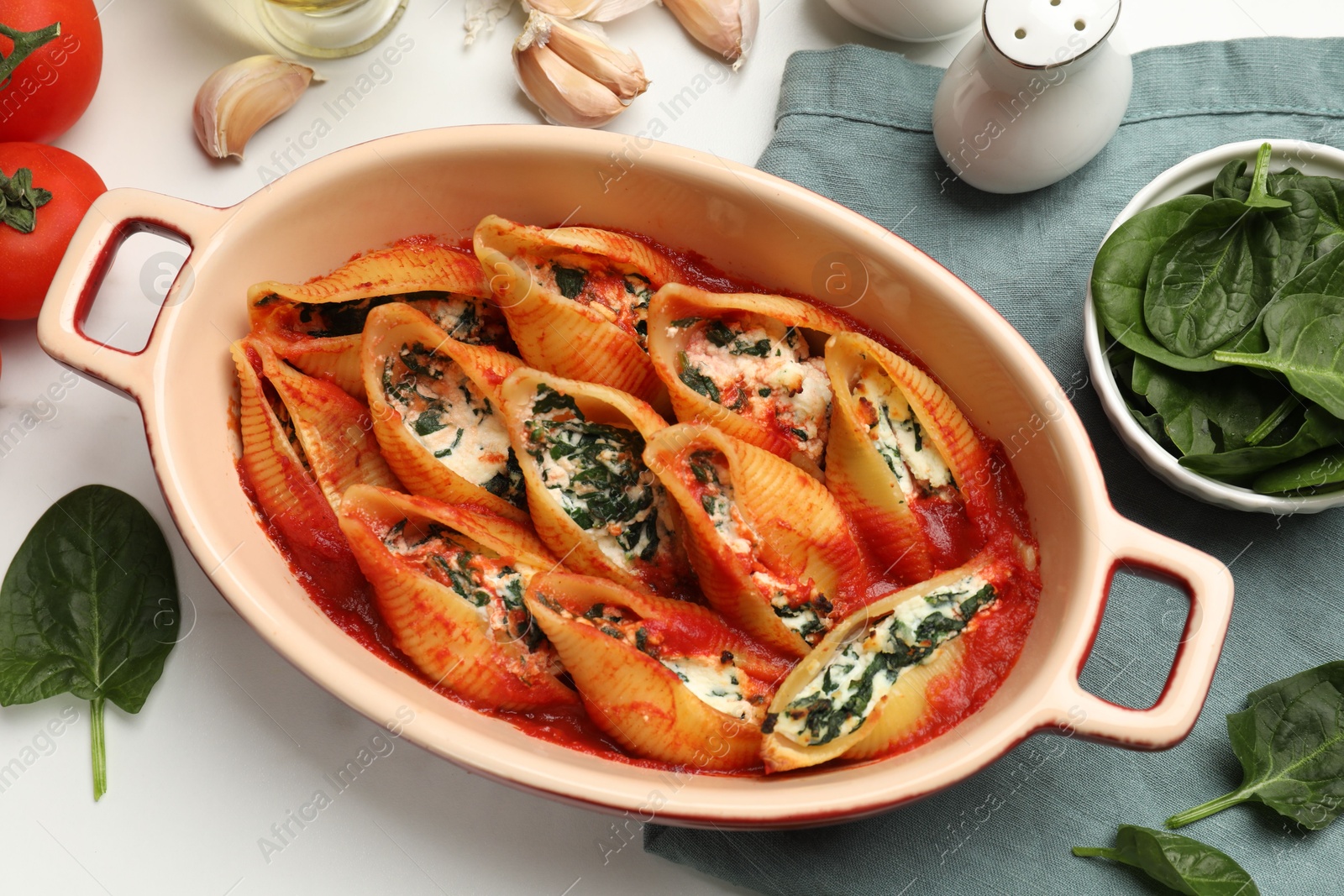 Photo of Delicious conchiglie pasta with ricotta cheese, spinach and tomato sauce in baking dish on white table, flat lay