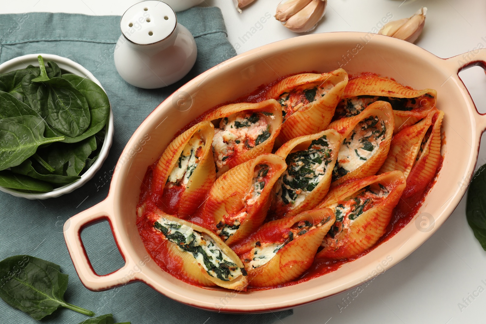 Photo of Delicious conchiglie pasta with ricotta cheese, spinach and tomato sauce in baking dish on white table, flat lay