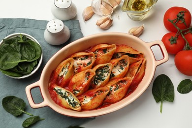 Photo of Delicious conchiglie pasta with ricotta cheese, spinach and tomato sauce in baking dish on white table, flat lay