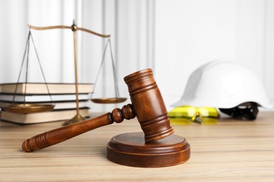 Photo of Accident at work. Gavel, safety equipment, scales and stack of books on wooden table, closeup