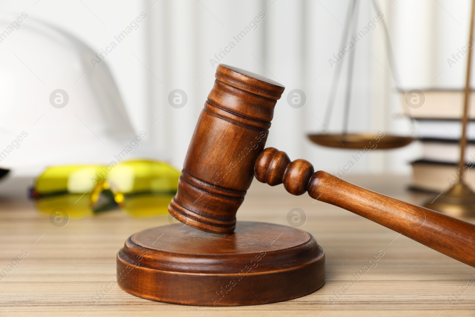 Photo of Accident at work. Gavel, safety equipment, scales and stack of books on wooden table, selective focus