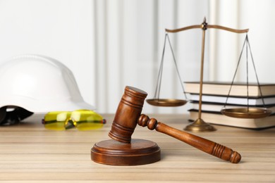 Photo of Accident at work. Gavel, safety equipment, scales and stack of books on wooden table, selective focus