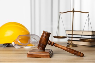 Photo of Accident at work. Gavel, safety equipment, scales and stack of books on wooden table, selective focus