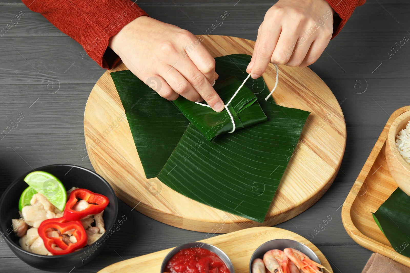 Photo of Woman tying banana leaf with food at wooden table with products, top view. Healthy eco serving