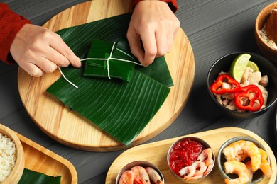 Photo of Woman tying banana leaf with food at wooden table with products, top view. Healthy eco serving