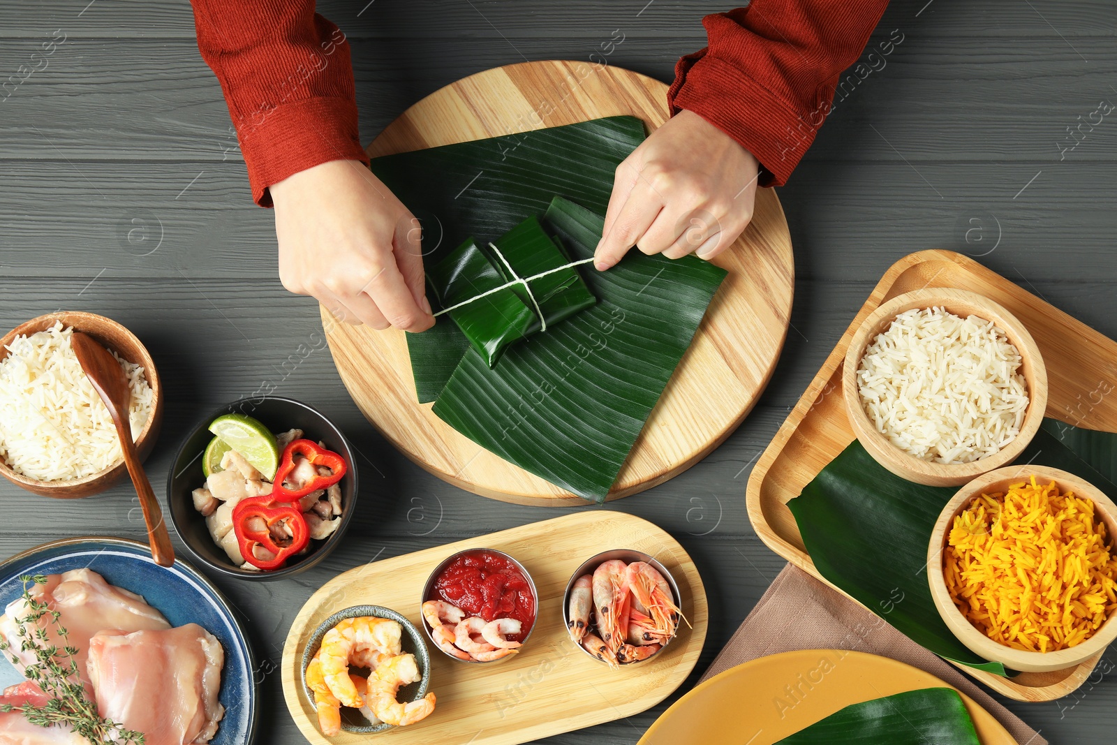 Photo of Woman tying banana leaf with food at wooden table with products, top view. Healthy eco serving