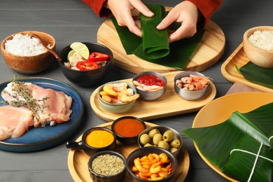 Photo of Woman wrapping food into banana leaf at wooden table with products, closeup. Healthy eco serving