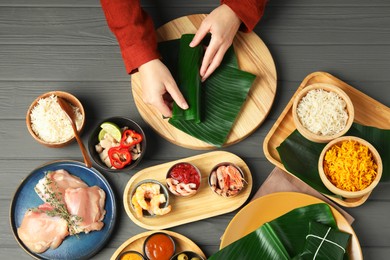 Photo of Woman wrapping food into banana leaf at wooden table with products, top view. Healthy eco serving