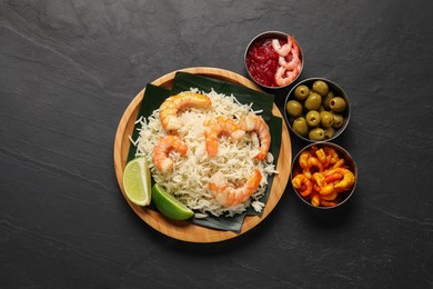 Photo of Pieces of banana leaf with rice, shrimps and lime among other food and sauce on grey textured table, flat lay