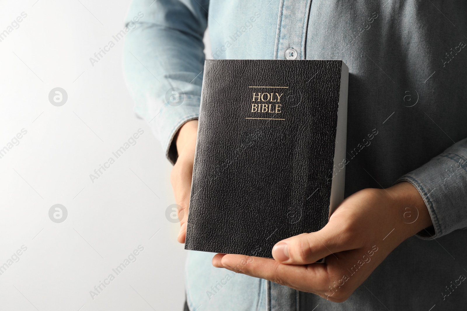 Photo of Man with hardcover Holy Bible on light background, closeup. Space for text