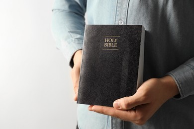 Man with hardcover Holy Bible on light background, closeup. Space for text