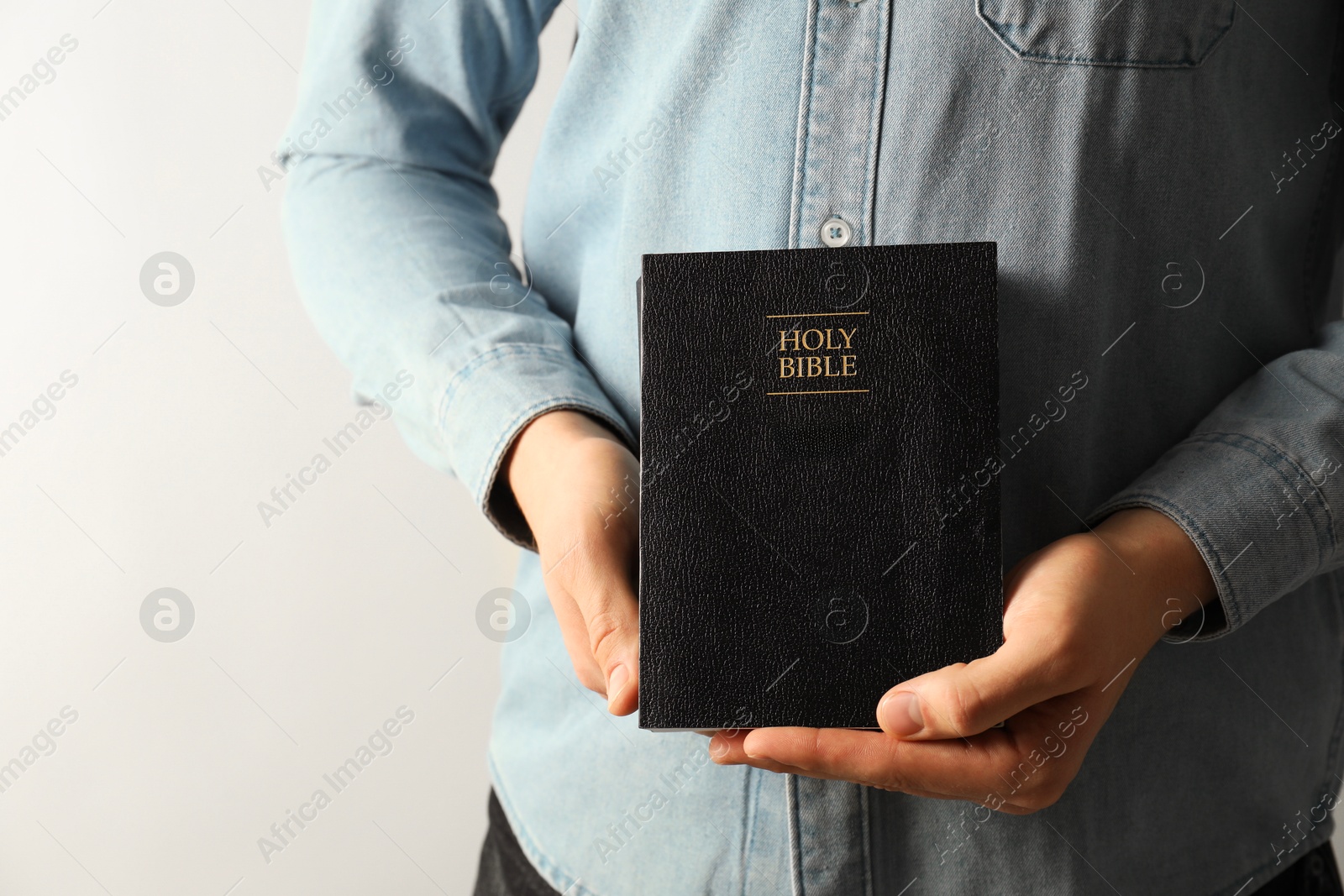 Photo of Man with hardcover Holy Bible on light background, closeup. Space for text