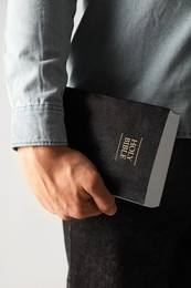 Photo of Man with hardcover Holy Bible on light background, closeup