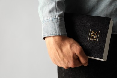 Man with hardcover Holy Bible on light background, closeup. Space for text