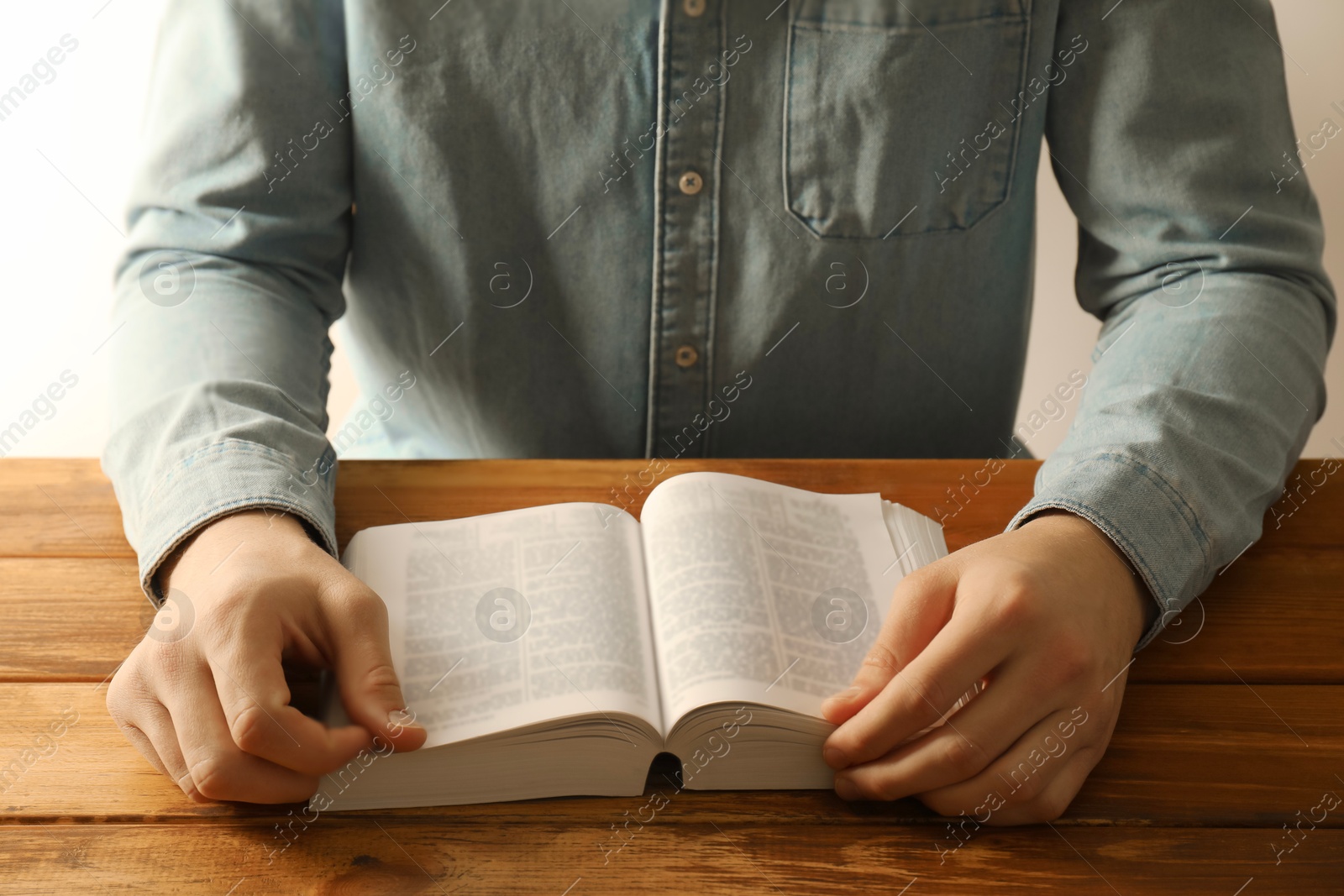 Photo of Man reading Holy Bible in English language at wooden table, closeup