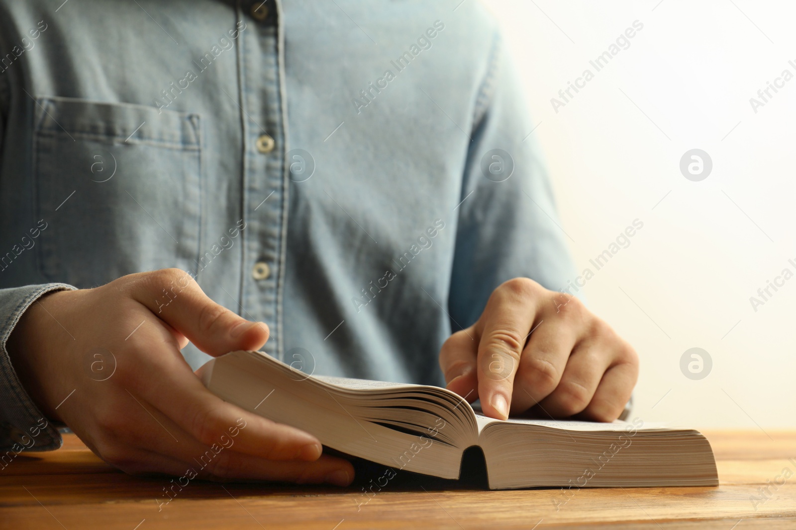 Photo of Man reading Holy Bible at wooden table, closeup