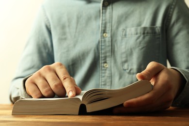 Man reading Holy Bible at wooden table, closeup