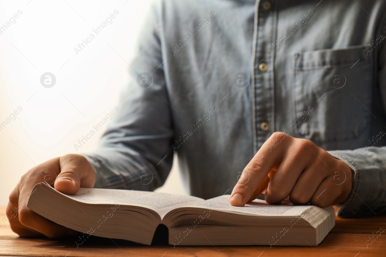 Photo of Man reading Holy Bible at wooden table, closeup