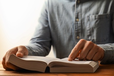 Man reading Holy Bible at wooden table, closeup