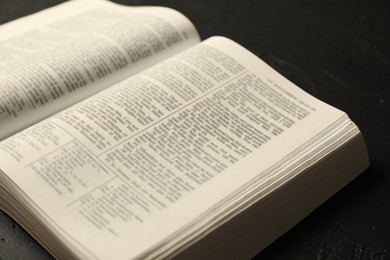 Photo of Open Holy Bible in English language on black table, closeup