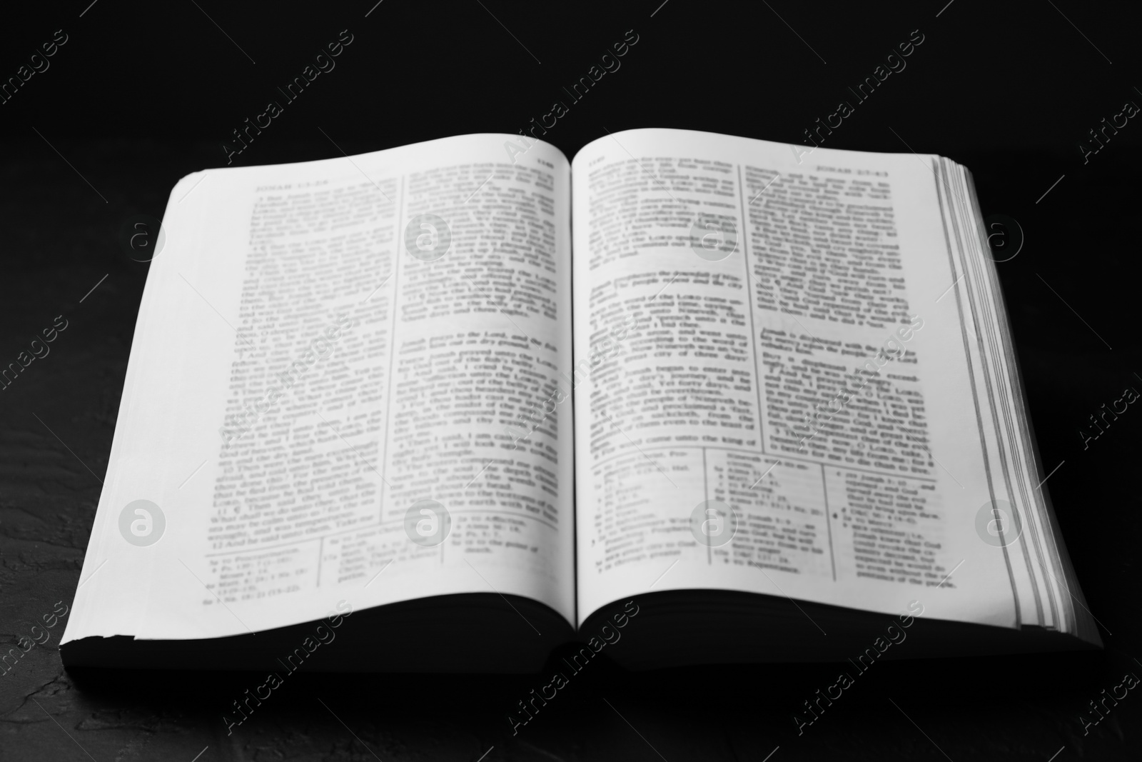 Photo of Open Holy Bible in English language on black table, closeup