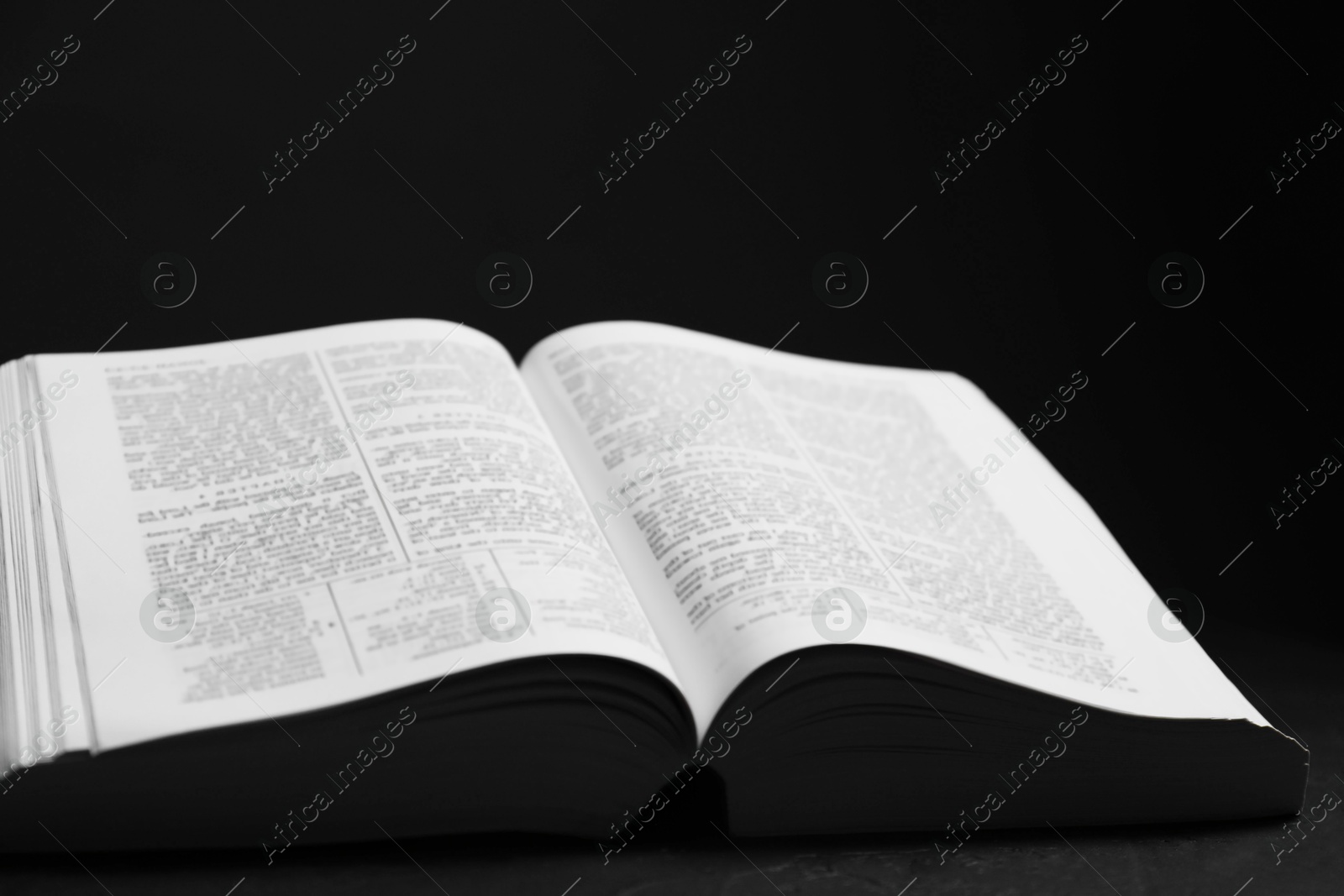 Photo of Open Holy Bible on black table, closeup