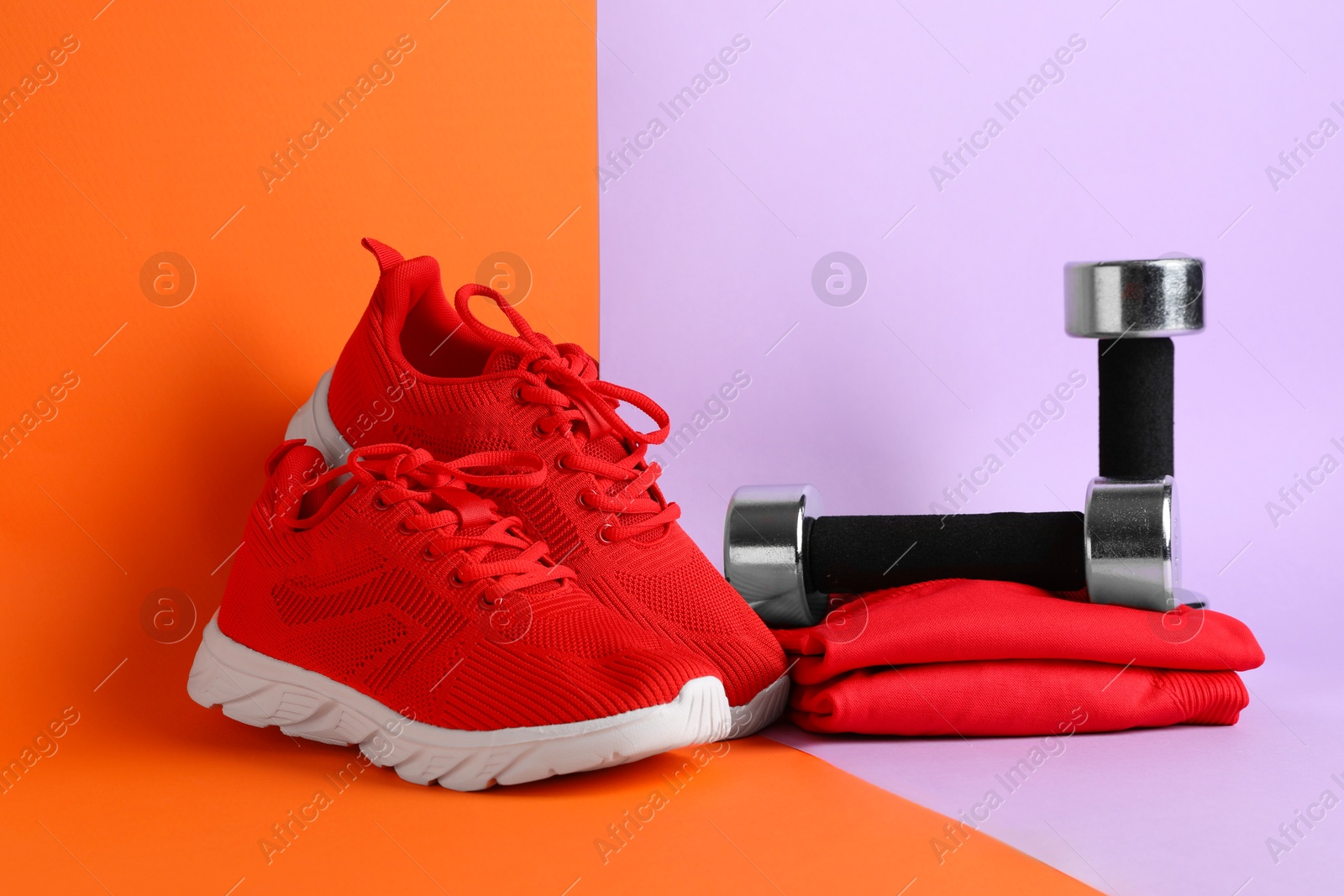 Photo of Pair of stylish red sneakers and dumbbells on color background