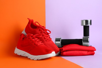 Photo of Pair of stylish red sneakers and dumbbells on color background