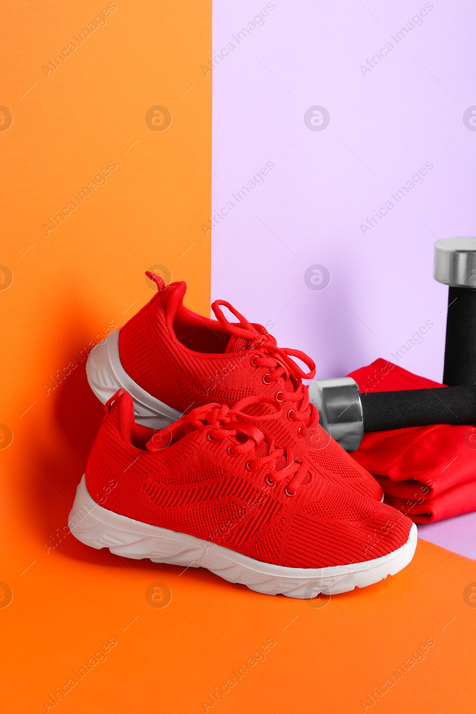 Photo of Pair of stylish red sneakers and dumbbells on color background