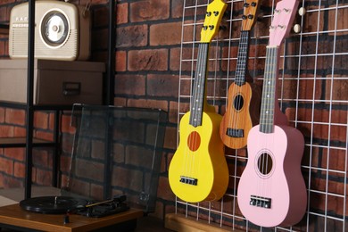 Photo of Three colorful ukulele on brick wall and record player indoors