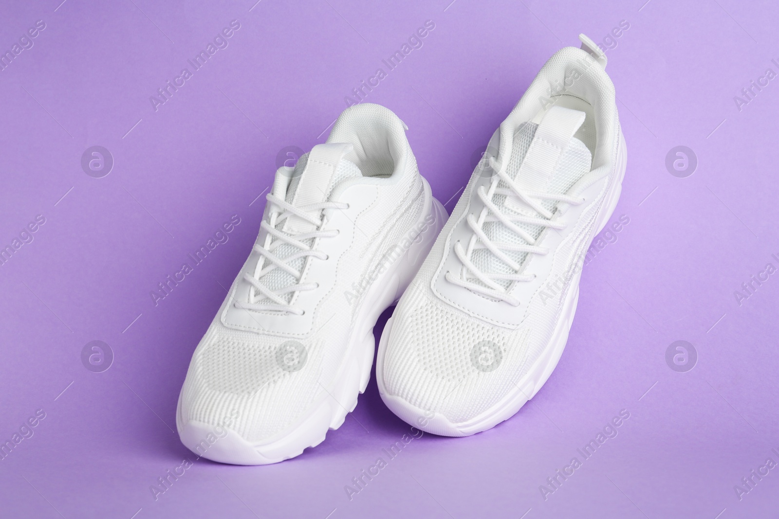 Photo of Pair of stylish white sneakers on violet background