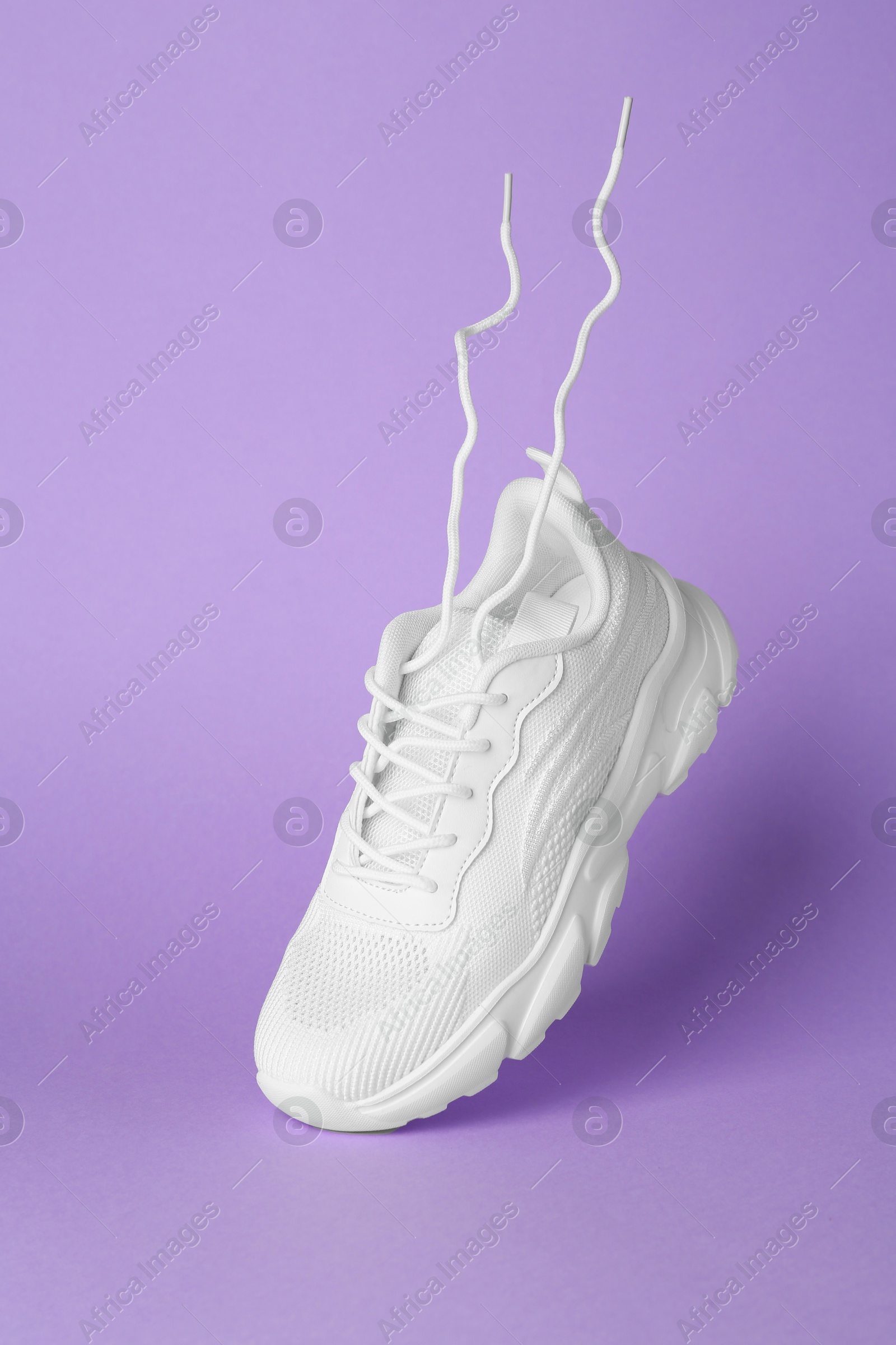 Photo of Stylish white sneaker in air against violet background